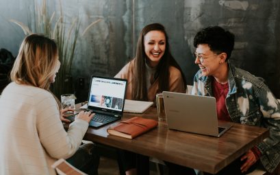 trois personnes autour d'une table avec ordinateur qui rigolent